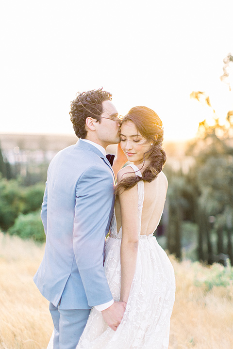  bridal hair with a french braid and crystal and the groom in a light blue suit kissing her head