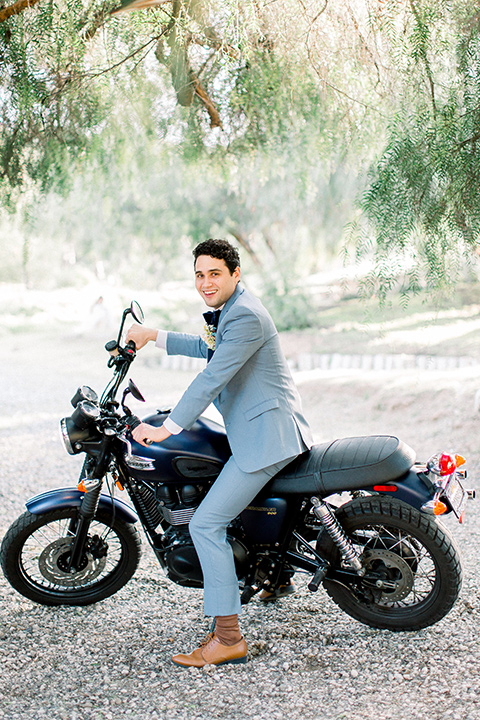  groom in a light blue suit and velvet bow tie on a motorcycle