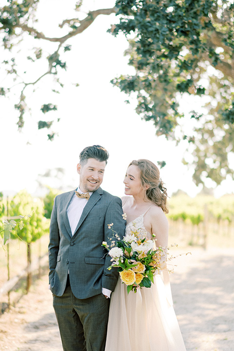  bride looking in a white flowing gown and the groom in a grey notch lapel suit with a gold velvet bow tie 