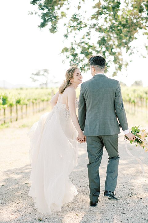  bride looking in a white flowing gown and the groom in a grey notch lapel suit with a gold velvet bow tie