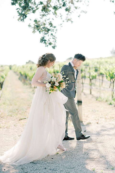  bride looking in a white flowing gown and the groom in a grey notch lapel suit with a gold velvet bow tie 