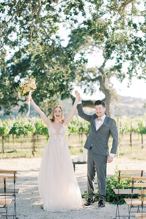  bride looking in a white flowing gown and the groom in a grey notch lapel suit with a gold velvet bow tie