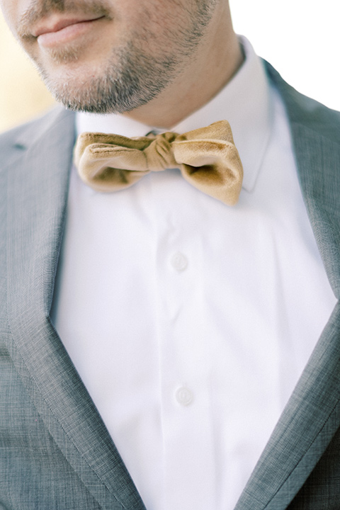  groom in a grey notch lapel suit with a gold velvet bow tie 