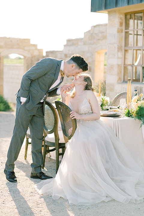  bride looking in a white flowing gown and the groom in a grey notch lapel suit with a gold velvet bow tie