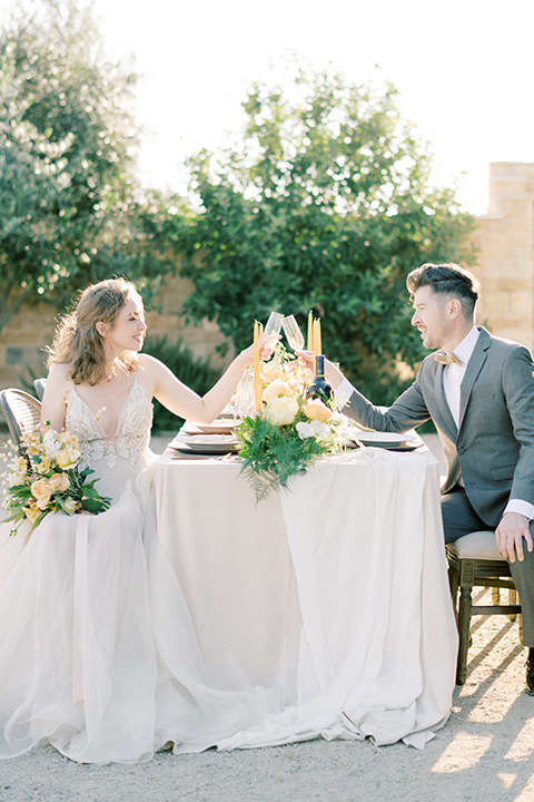  bride looking in a white flowing gown and the groom in a grey notch lapel suit with a gold velvet bow tie 