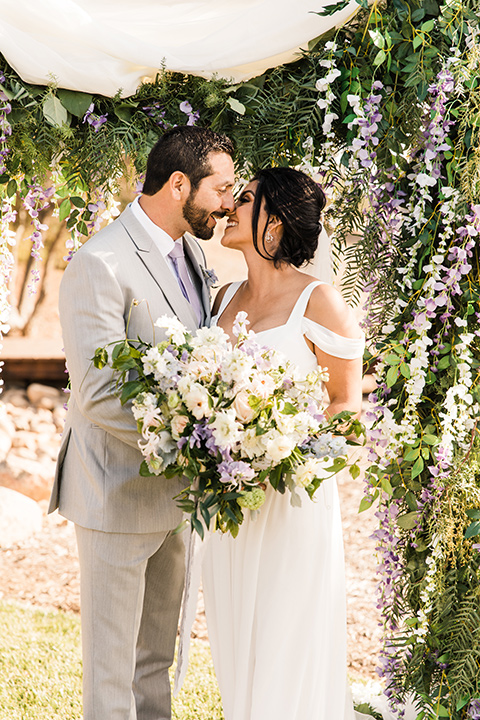  bride in a white flowing gown with off the shoulder detailing and the groom in a light grey suit with a lavender long tie