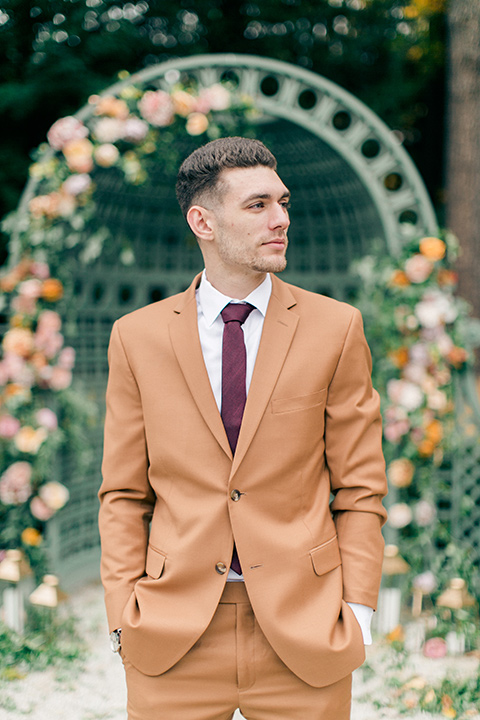  the groom is in a caramel rust colored suit with a dark brown long tie