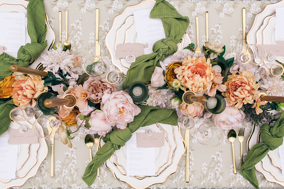  table with white linens and green napkins, tall orange candles and green and pink cascading flowers 