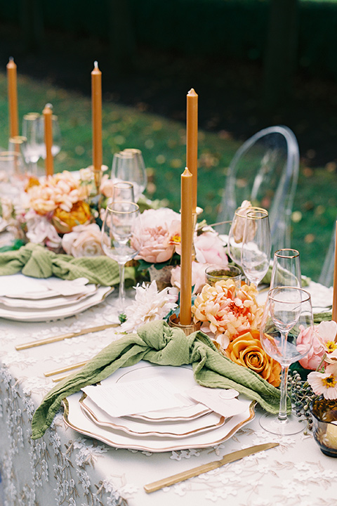  table with white linens and green napkins and orange tall candles