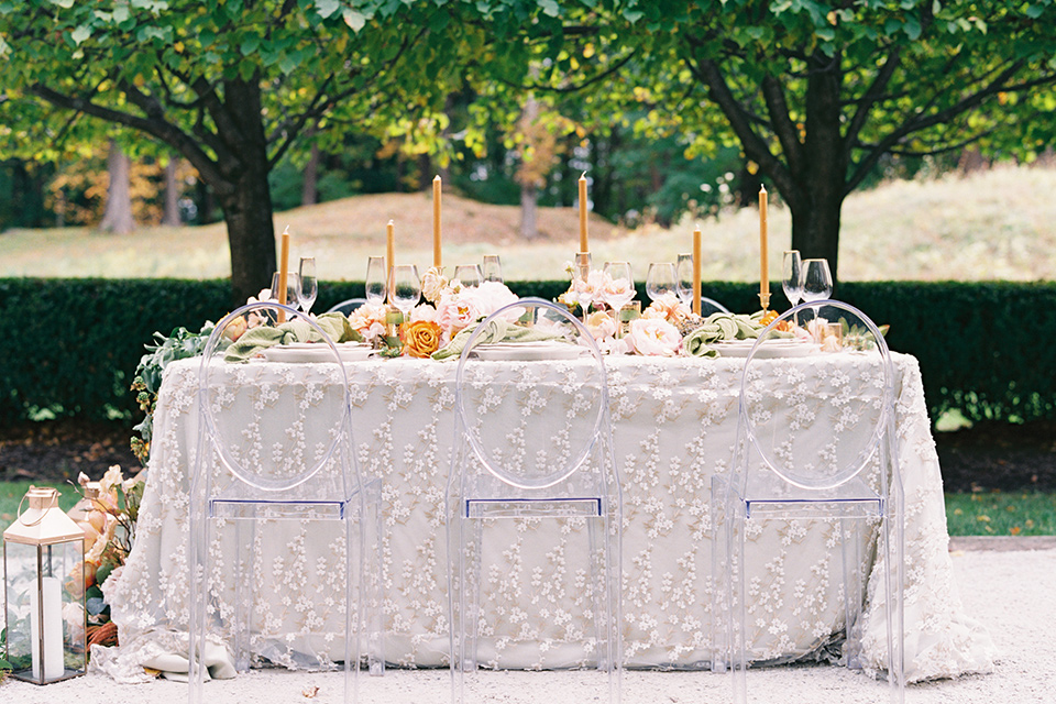  table with white linens and green napkins, tall orange candles and green and pink cascading flowers 