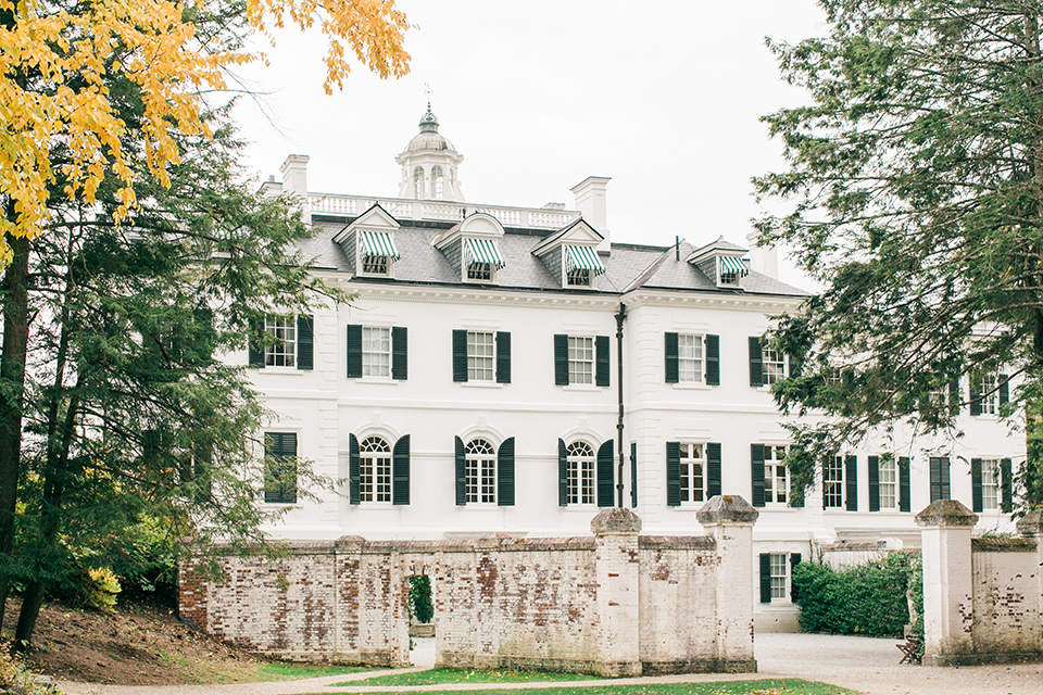  white Victorian mansion with black shutters and tall green trees 