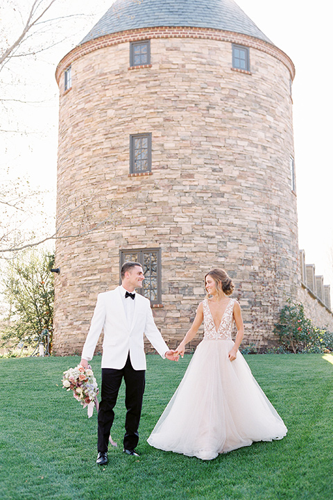  bride in a long flowing gown with long sleeves and a plunging neckline and the groom in a white tuxedo and black pants and bow tie, by brick tower 