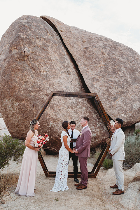  bride in a boho two-piece gown and groom in a pink suit with long tie, bridesmaid in a neutral gown and groomsman in a tan suit