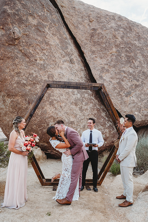  bride in a boho two-piece gown and groom in a pink suit with long tie, bridesmaid in a neutral gown and groomsman in a tan suit 