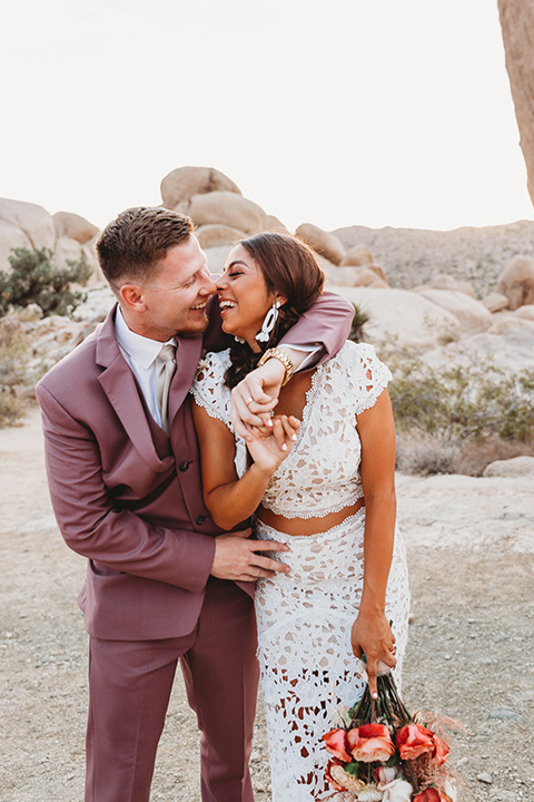 bride in a boho two-piece gown and groom in a pink suit with long tie, bridesmaid in a neutral gown and groomsman in a tan suit