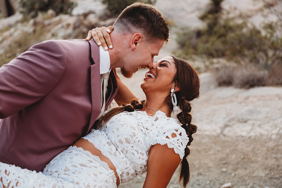  groom in a pink suit with long tie and the bride in a two piece white lace gown