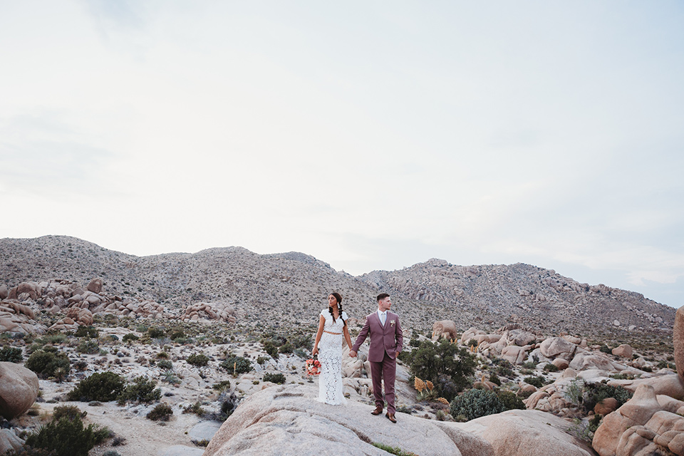  groom in a pink suit with long tie and the bride in a two piece white lace gown