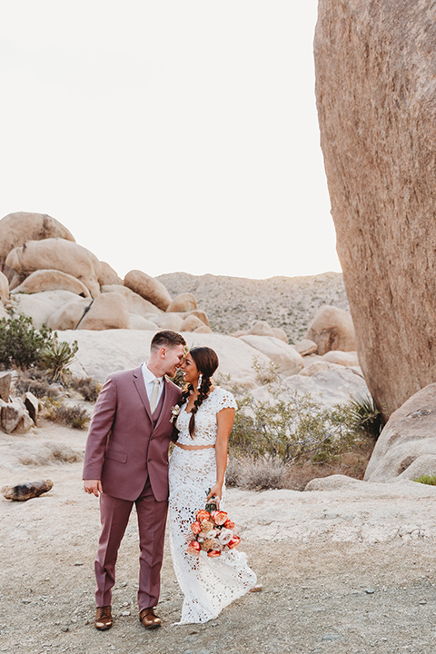  bride in a boho two-piece gown and groom in a pink suit with long tie, bridesmaid in a neutral gown and groomsman in a tan suit 