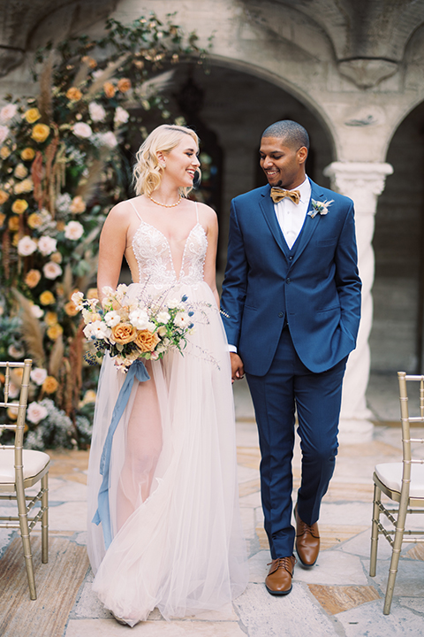  bride in a modern bohemian gown with a sheer skirt and crystal embellishments and the groom in a dark blue suit and a gold velvet bow tie