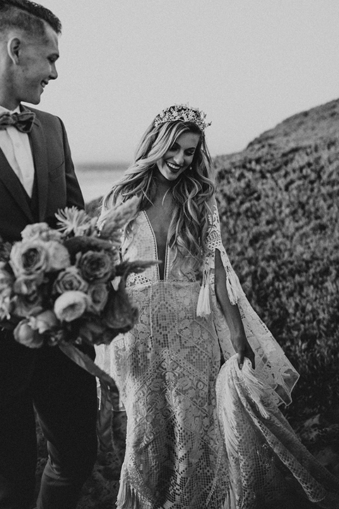  bride in a lace long sleeve gown with a plunging neckline and a boho headpiece and the groom in a rose pink suit with a gold velvet bow tie