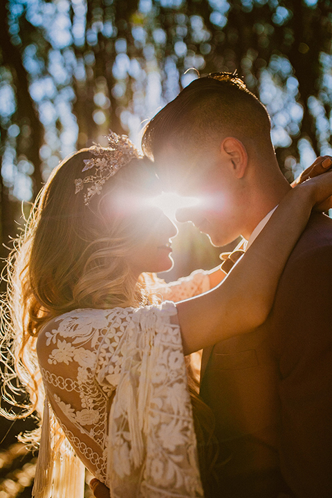  bride in a lace long sleeve gown with a plunging neckline and a boho headpiece and the groom in a rose pink suit with a gold velvet bow tie