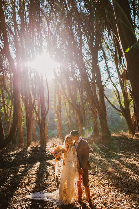  bride in a lace long sleeve gown with a plunging neckline and a boho headpiece and the groom in a rose pink suit with a gold velvet bow tie 