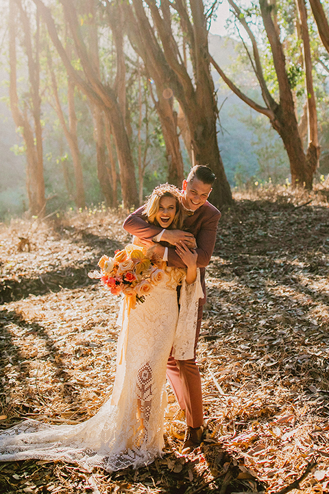  bride in a lace long sleeve gown with a plunging neckline and a boho headpiece and the groom in a rose pink suit with a gold velvet bow tie 