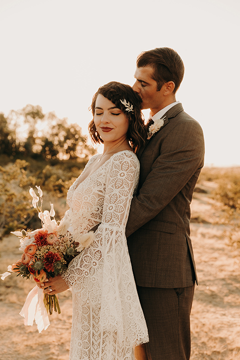  bride in a bohemian lace gown with flutter sleeves and a hat and the groom in a café brown suit with a chocolate long tie