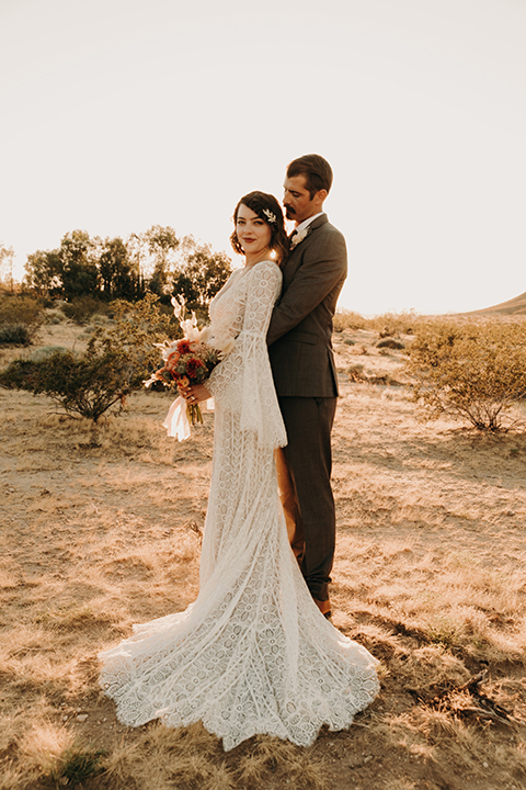   bride in a bohemian lace gown with flutter sleeves and a hat and the groom in a café brown suit with a chocolate long tie 