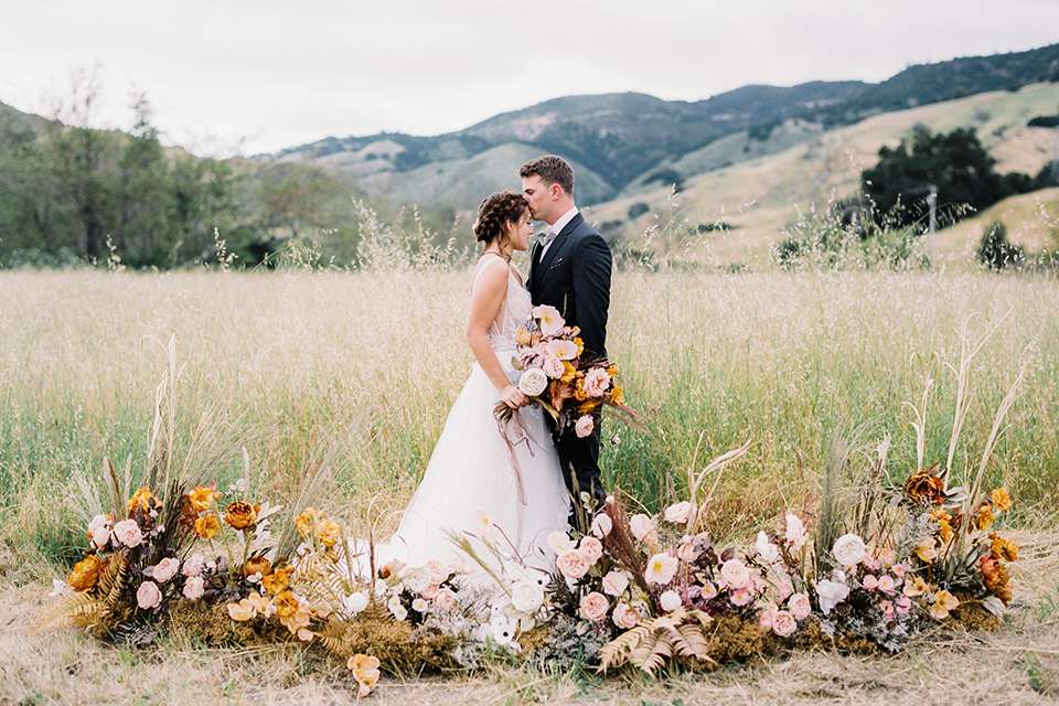  bride in a flowing bohemian gown with her hair in a loose braided bun and flowers and the groom in an asphalt grey suit 