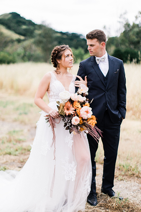  bride in a flowing bohemian gown with her hair in a loose braided bun and flowers and the groom in an asphalt grey suit