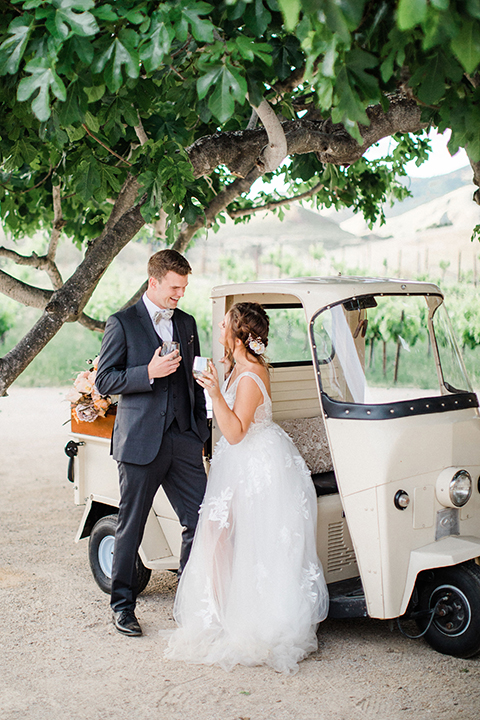  bride in a flowing bohemian gown with her hair in a loose braided bun and flowers and the groom in an asphalt grey suit 