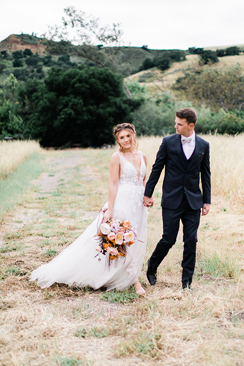 bride in a flowing bohemian gown with her hair in a loose braided bun and flowers and the groom in an asphalt grey suit 