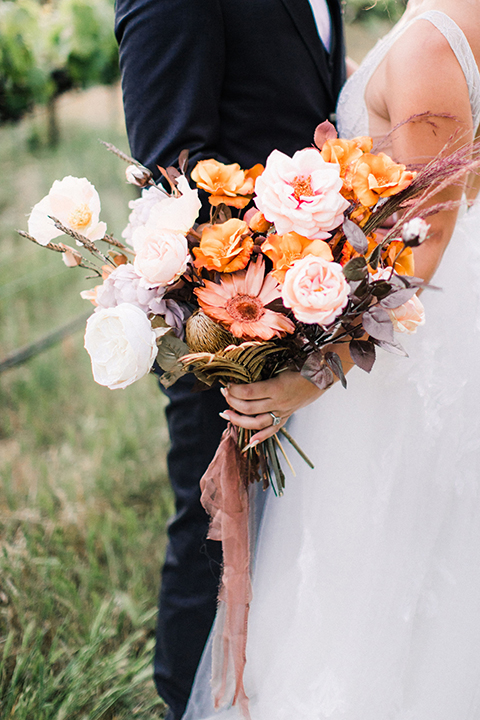  bride in a flowing bohemian gown with her hair in a loose braided bun and flowers and the groom in an asphalt grey suit 