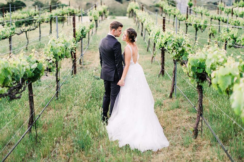  bride in a flowing bohemian gown with her hair in a loose braided bun and flowers and the groom in an asphalt grey suit 