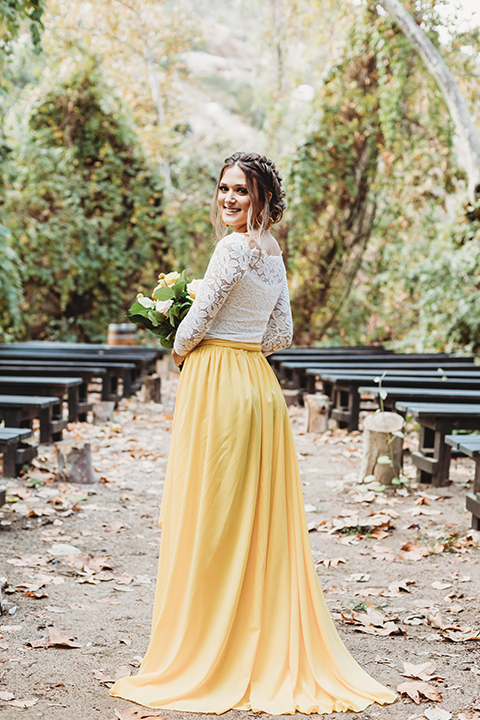  groom in an ivory paisley tuxedo and gold velvet bow tie and the bride in a two-piece gown with a yellow skirt and ivory long sleeve top 