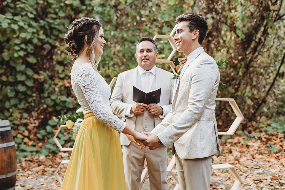  groom in an ivory paisley tuxedo and gold velvet bow tie and the bride in a two-piece gown with a yellow skirt and ivory long sleeve top 