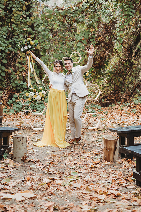  groom in an ivory paisley tuxedo and gold velvet bow tie and the bride in a two-piece gown with a yellow skirt and ivory long sleeve top 