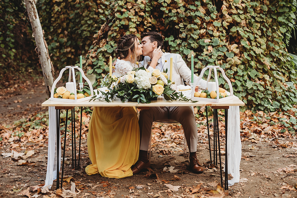  groom in an ivory paisley tuxedo and gold velvet bow tie and the bride in a two-piece gown with a yellow skirt and ivory long sleeve top 