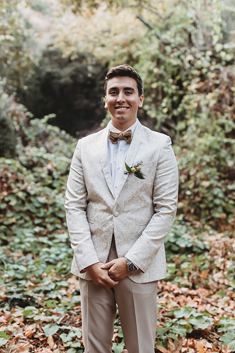   groom in an ivory paisley tuxedo and gold velvet bow tie and the bride in a two-piece gown with a yellow skirt and ivory long sleeve top 