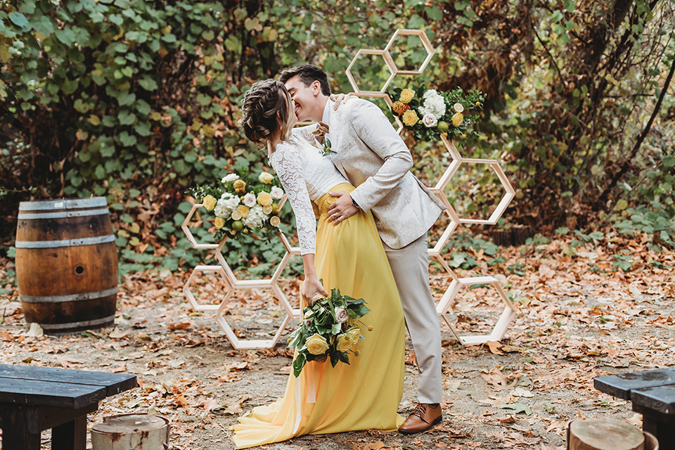  groom in an ivory paisley tuxedo and gold velvet bow tie and the bride in a two-piece gown with a yellow skirt and ivory long sleeve top 