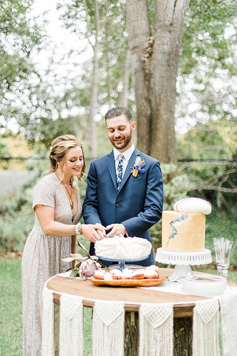  bride in an ivory and champagne gown with sleeves and the groom in a blue suit with a blue floral neck tie 