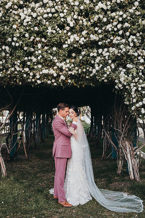  bride in a flowing lace gown and the groom in a rose pink suit