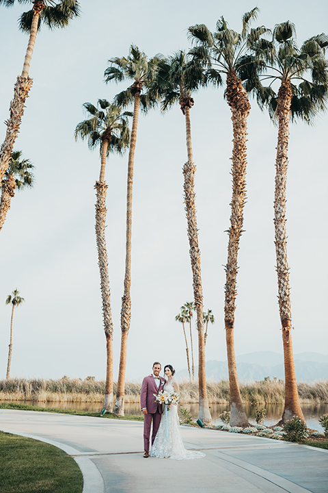  bride in a flowing lace gown and the groom in a rose pink suit