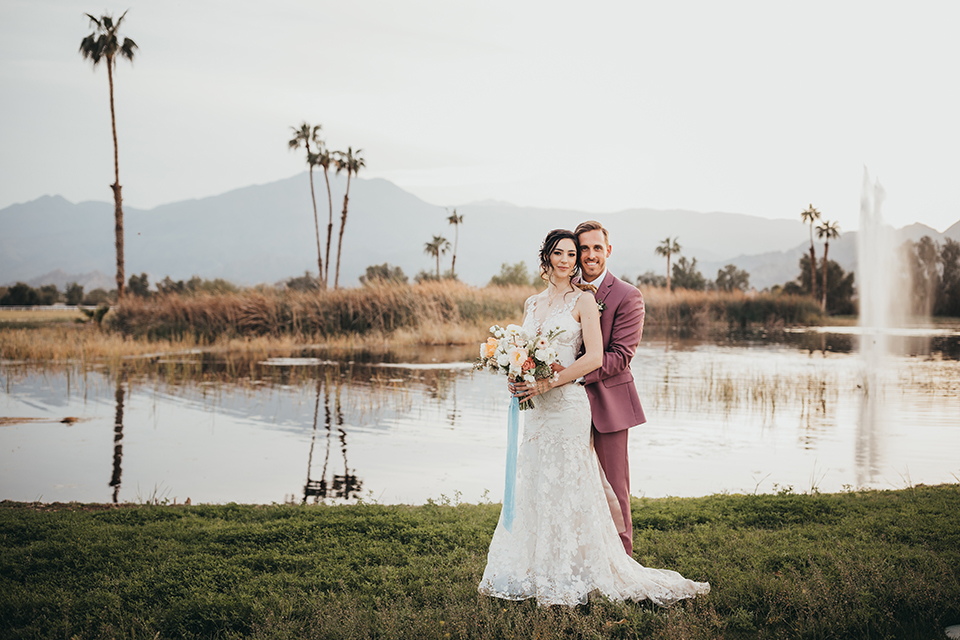  bride in a flowing lace gown and the groom in a rose pink suit 