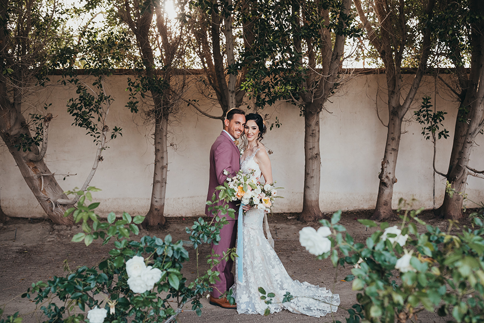  bride in a flowing lace gown and the groom in a rose pink suit 