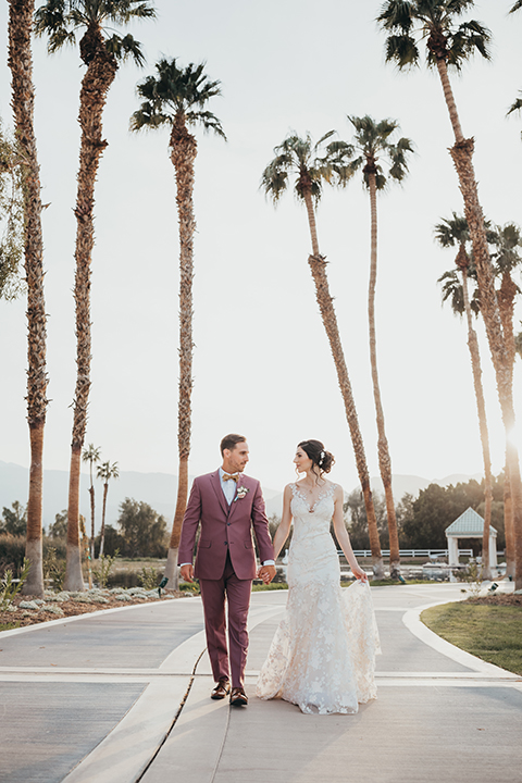  bride in a flowing lace gown and the groom in a rose pink suit 