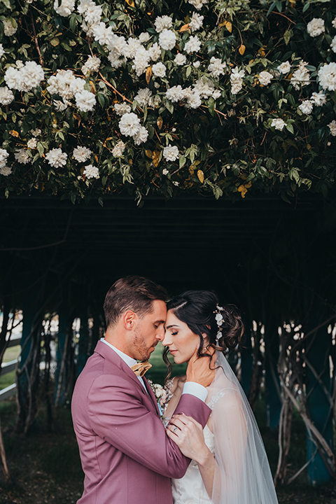  bride in a flowing lace gown and the groom in a rose pink suit 