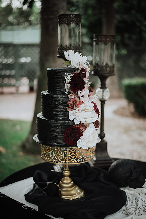  bride in a black gown with a black veil and the groom in a burgundy tuxedo with a black shirt and bow tie 