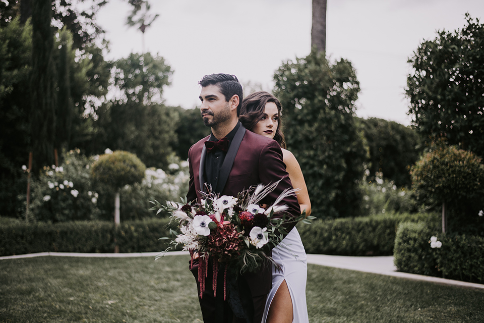  bride in a black gown with a black veil and the groom in a burgundy tuxedo with a black shirt and bow tie 